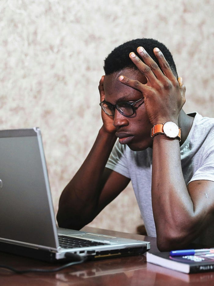 A black man with his hands held to his head, looking at a laptop and being stressed. A black man with his hands held to his head, looking at a laptop and being stressed.