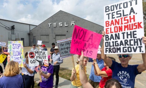 people hold signs outside a Tesla building that say 'Nola says no to Nazis' and 'Boycott Tesla, banish Elon Musk, ban the oligarchy from govt'