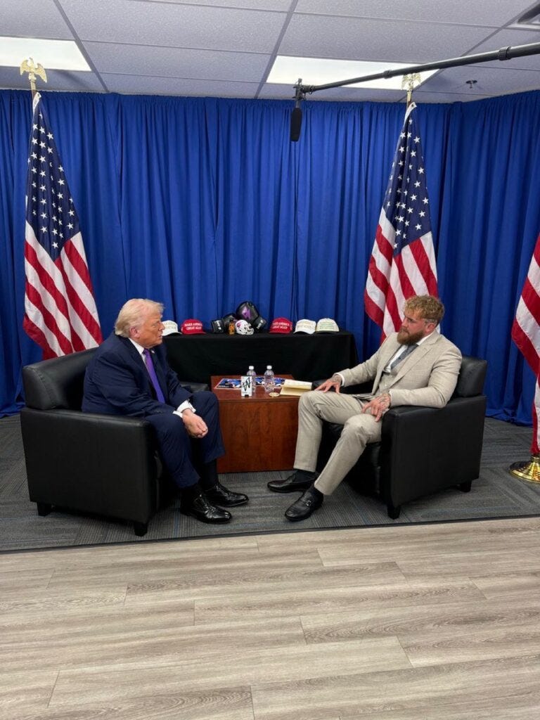 Two men in formal suits sitting on black leather chairs discussing in official government setting with American flags