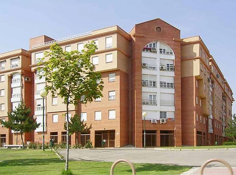 Un gruppo di edifici di case popolari a Getafe: le facciate sono fatte di mattoncini rossi, hanno tutte cinque piani e gli infissi bianchi. Di fronte, delle aiuole verdi con qualche albero sottile. Un gruppo di edifici di case popolari a Getafe: le facciate sono fatte di mattoncini rossi, hanno tutte cinque piani e gli infissi bianchi. Di fronte, delle aiuole verdi con qualche albero sottile.