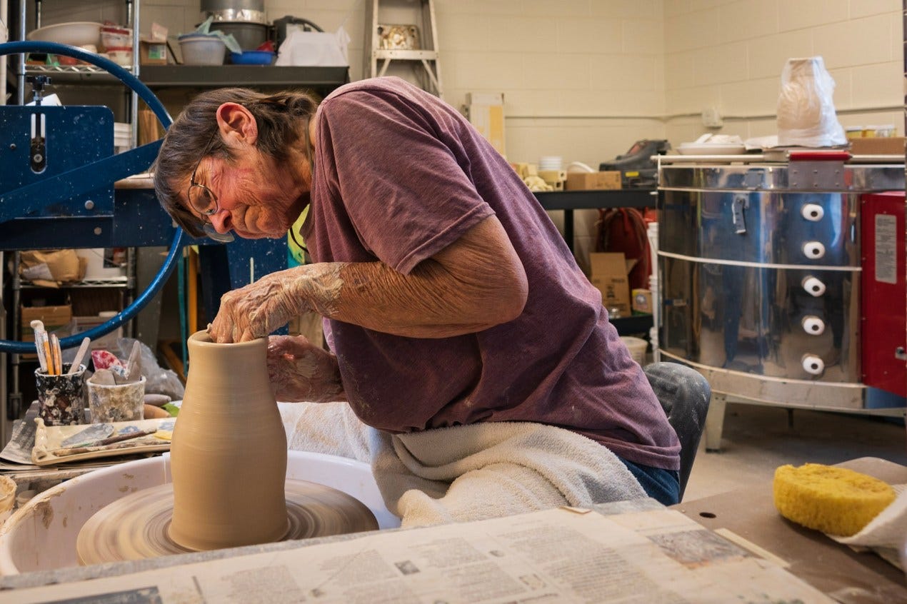 Denise Baker, a senior woman, works at a pottery wheel in a ceramics studio space. Denise Baker, a senior woman, works at a pottery wheel in a ceramics studio space.