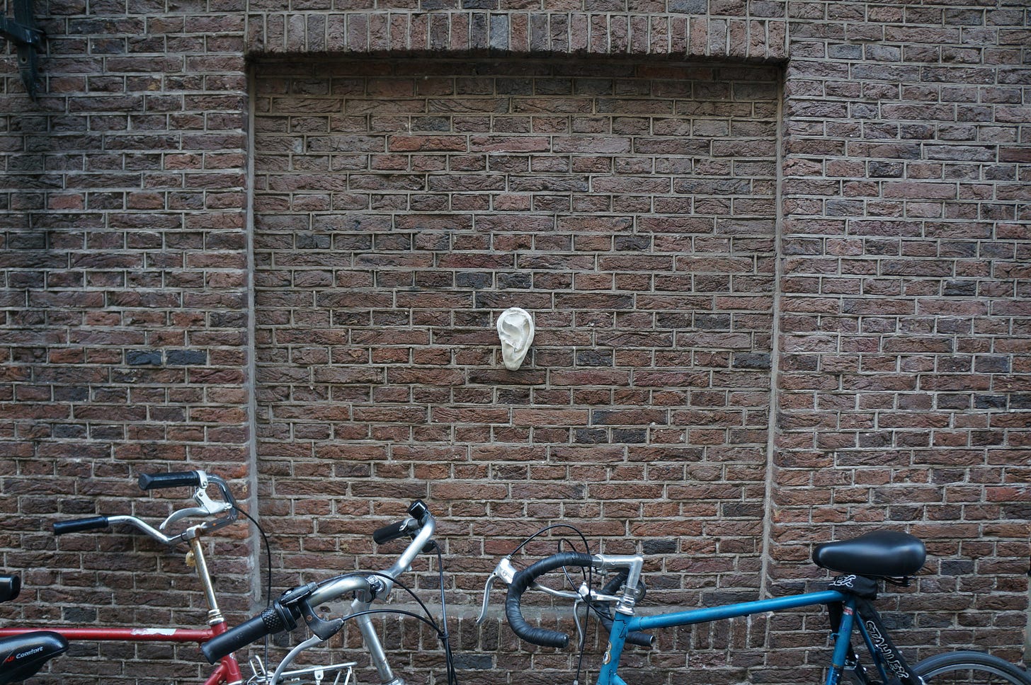 A photo of a sculpture of an ear on a brick wall in front of three bikes taken by the author in Amsterdam