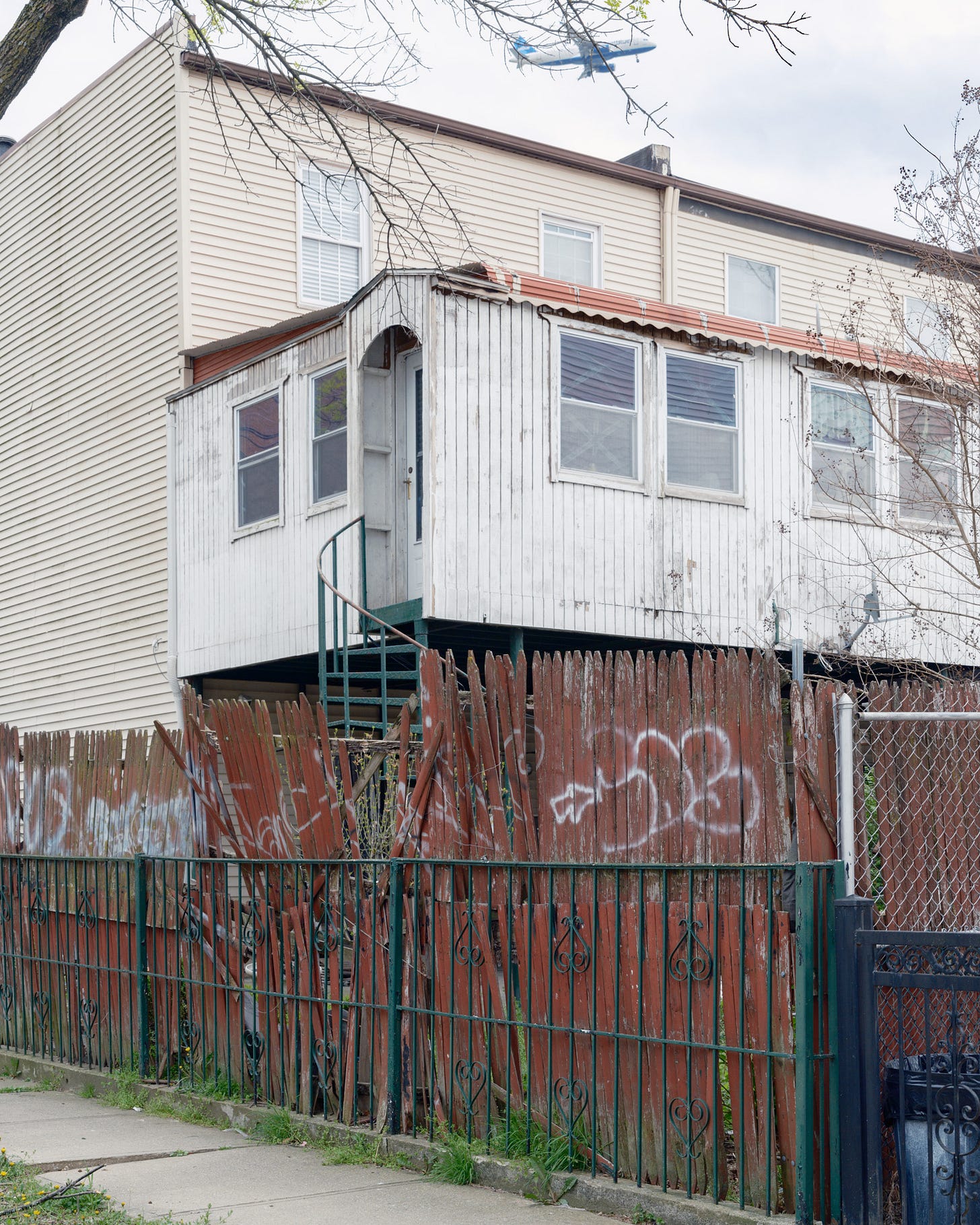 Vertical-Of-Two-Houses-One-With-A-Spiral-Staircase-Behind-A-Dilapidated-Red-Picket-Fence