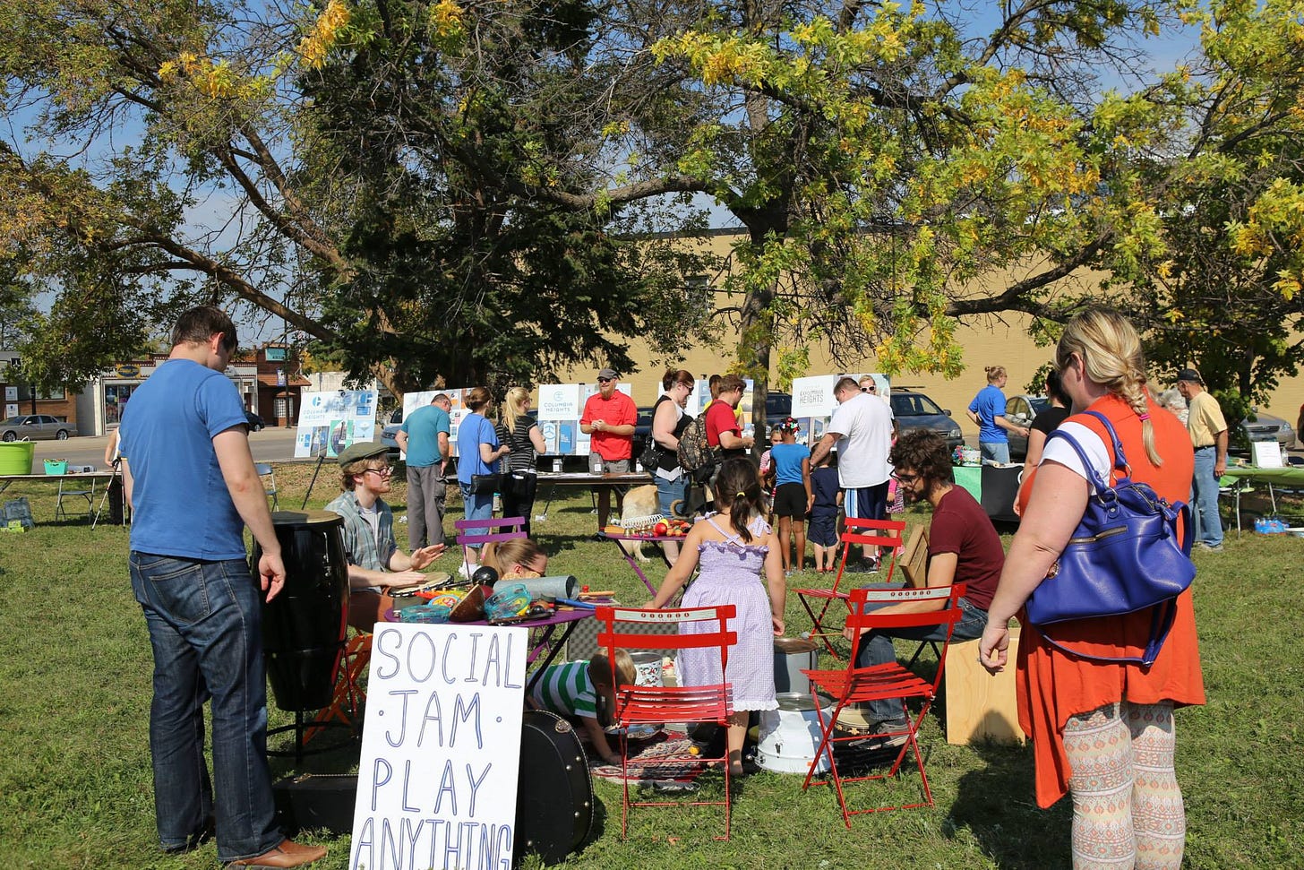 A crowd of people gather to play music and learn about a placemaking project at an event being held in a park.