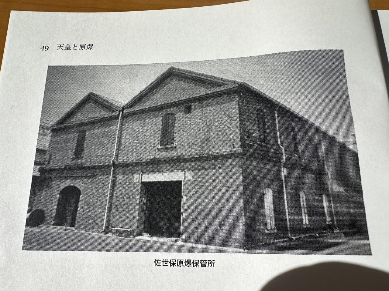 A black and white photograph of an old stone building with dormer windows and windows of varying sizes. A large entrance is located in the center of the building. A gravel area lies in front of the building.