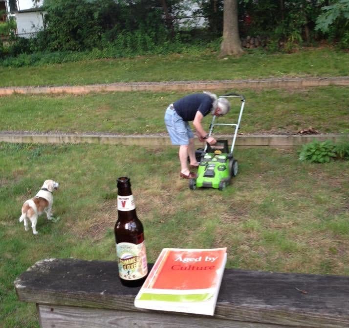 A man with a long white ponytail begins to mow the lawn. A beagle watches. 
