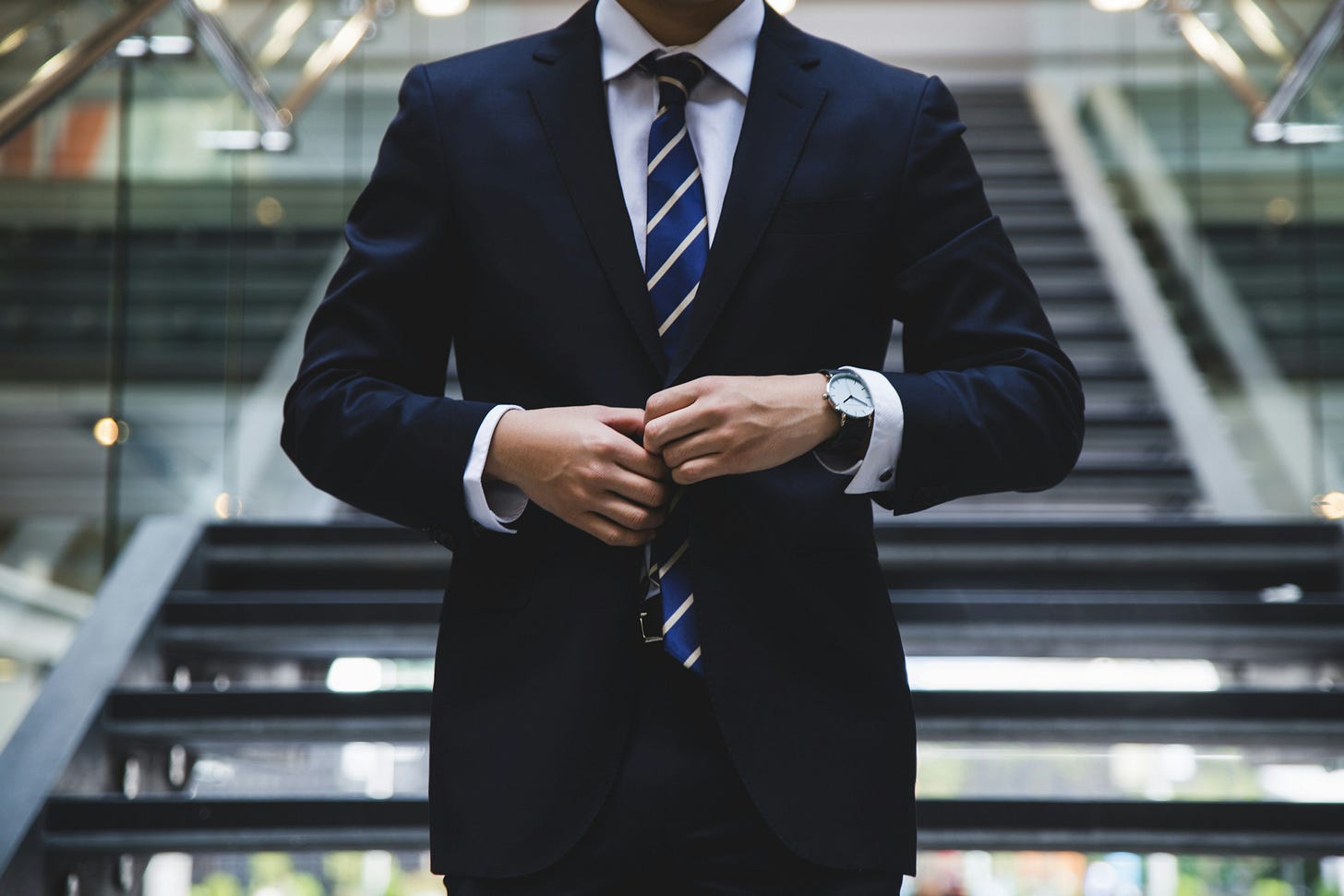 Professional in navy suit adjusting jacket in modern corporate office building stairwell