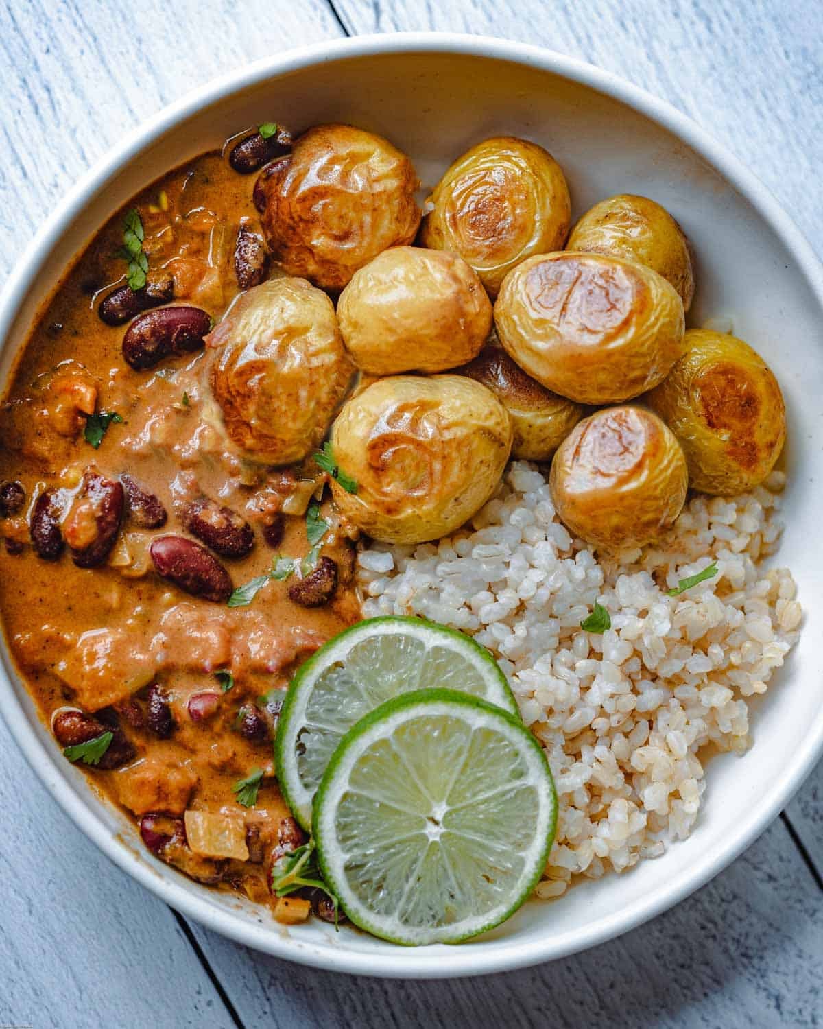 Bean curry with roasted potatoes, brown rice, lime, and cilantro in a bowl.