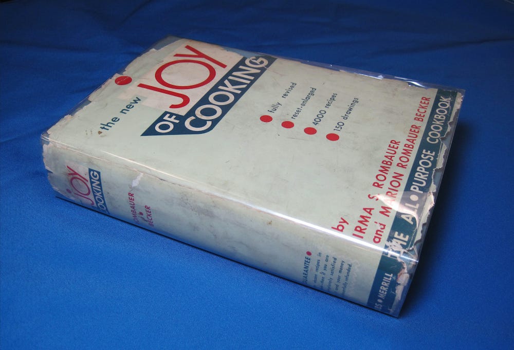A beat up first edition copy of The New Joy of Cooking with a clear cellophane jacket, on a blue cloth background. A beat up first edition copy of The New Joy of Cooking with a clear cellophane jacket, on a blue cloth background.