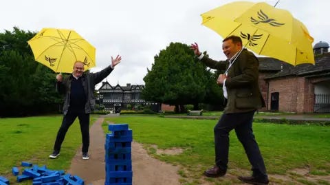 PA Media O líder dos Democratas Liberais, Sir Ed Davey, e o candidato parlamentar dos Democratas Liberais por Cheadle, Tom Morrison, tocam Jenga durante uma visita a Cheadle