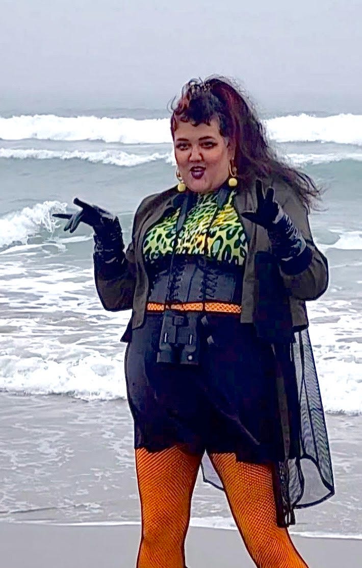 a Sri Lankan and white nb femme boss bitch in black, leopard print and orange fishnets make the cat hands pose in front of the atlantic ocean