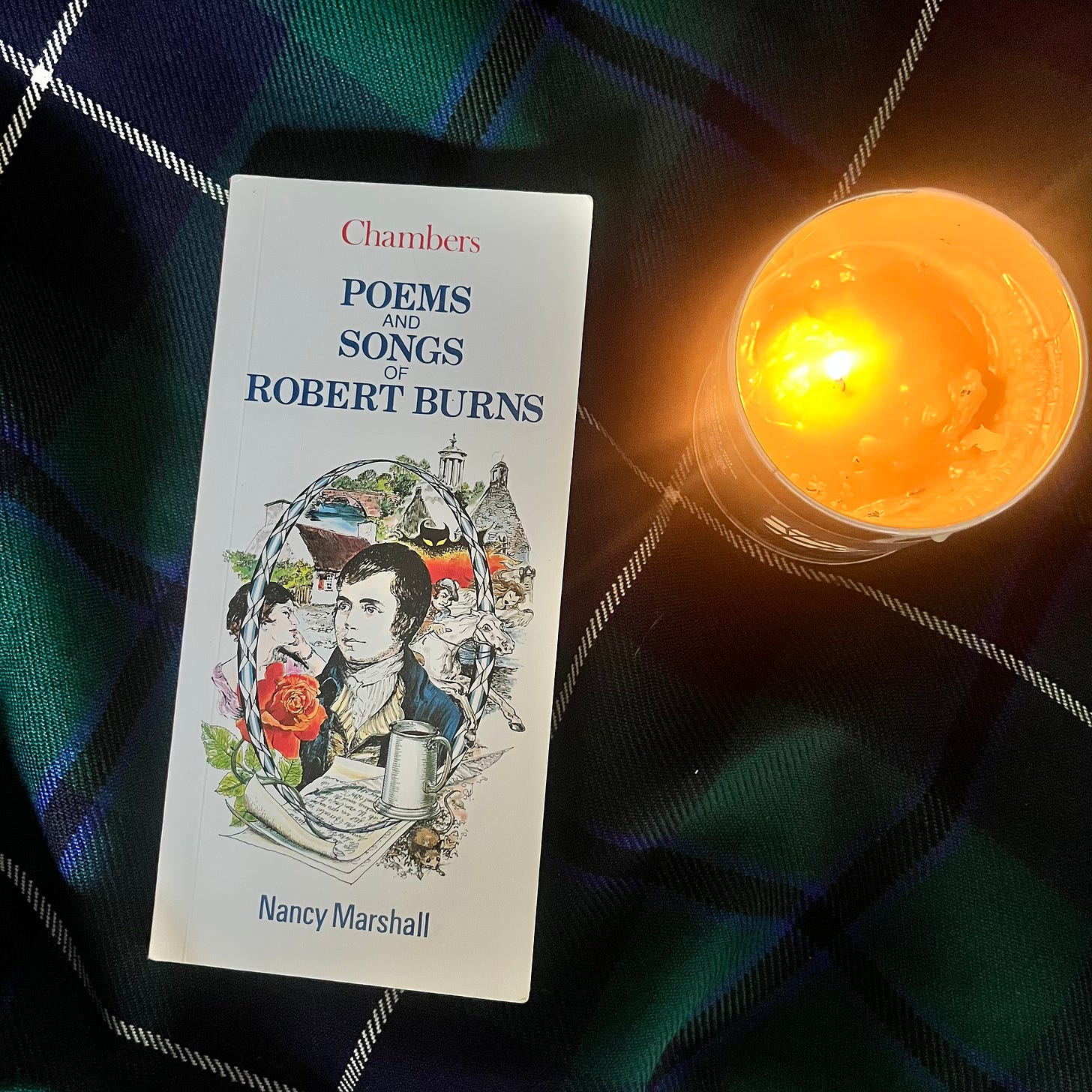 Robert Burns poetry book on tartan with a lit candle flickering 