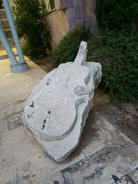 Three large stone sculptures in front of the Bet Musika: a half-guitar/half-cello; a viol, and a guitar with the faces of three musicians surrounding the instrument's neck.