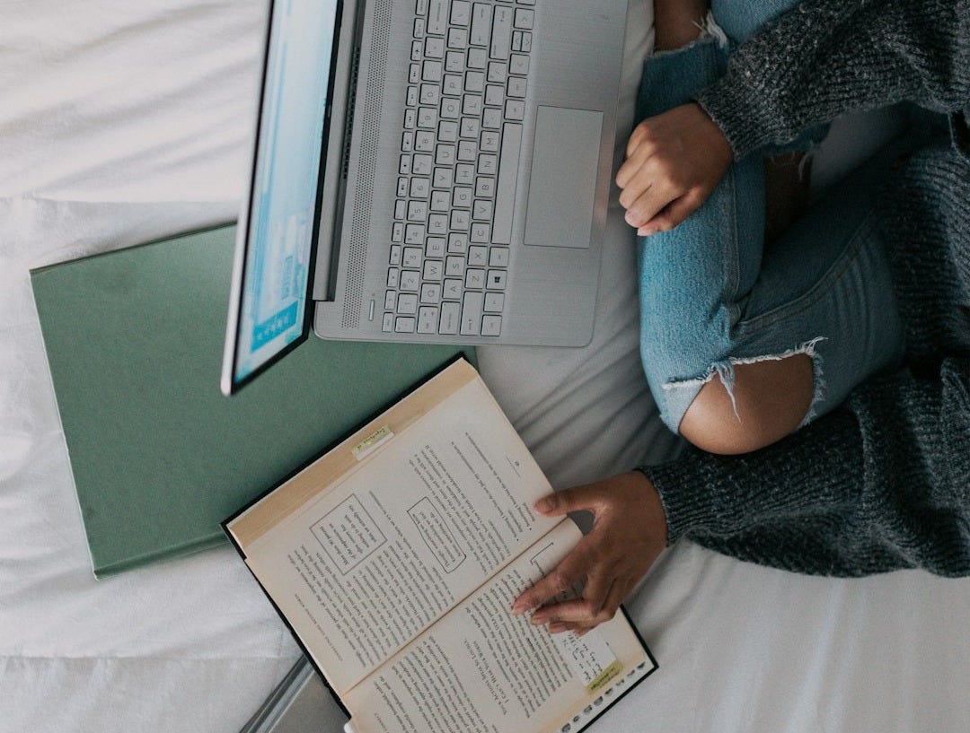 woman in blue long sleeve shirt and blue denim jeans sitting on bed using laptop
