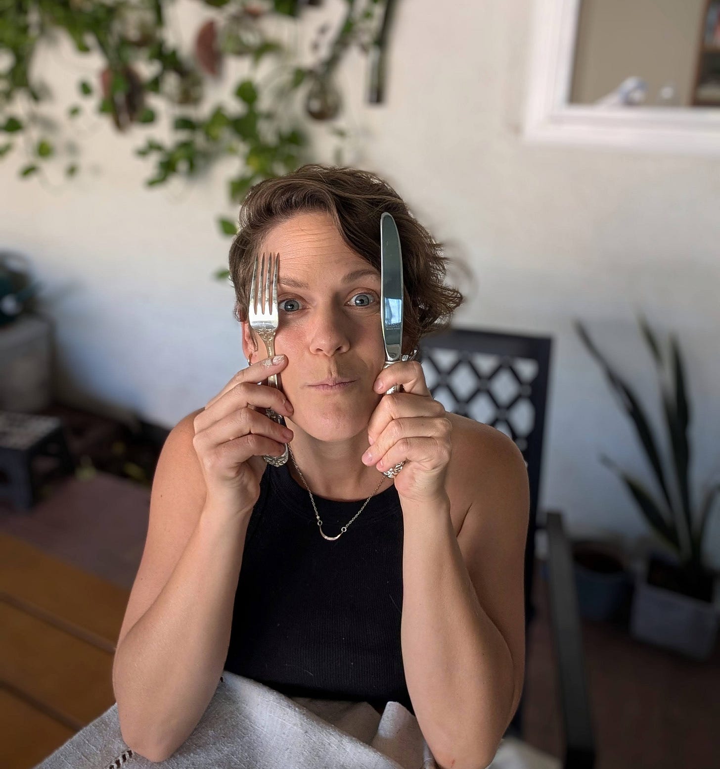Caroline holding a silver fork and knife up beside her face, looking at camera Caroline holding a silver fork and knife up beside her face, looking at camera