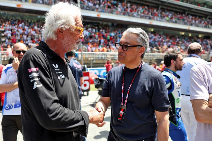 Flavio Briatore and Luca de Meo shaking hands at a Formula 1 race.