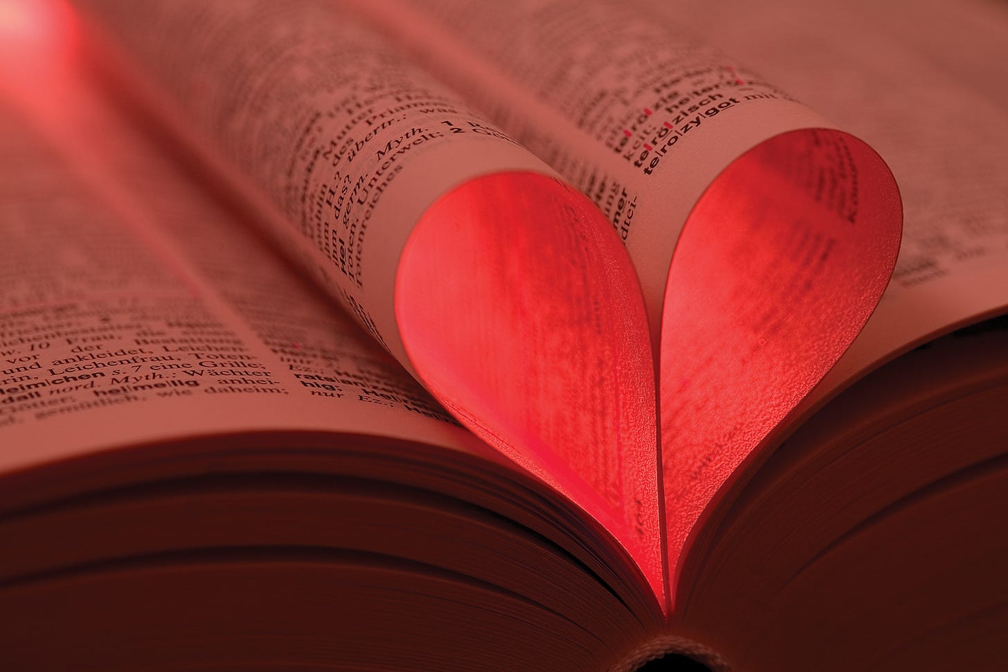 open pages of a book with words on all pages, two center pages folded into the shape of a heart, illuminated soft red open pages of a book with words on all pages, two center pages folded into the shape of a heart, illuminated soft red