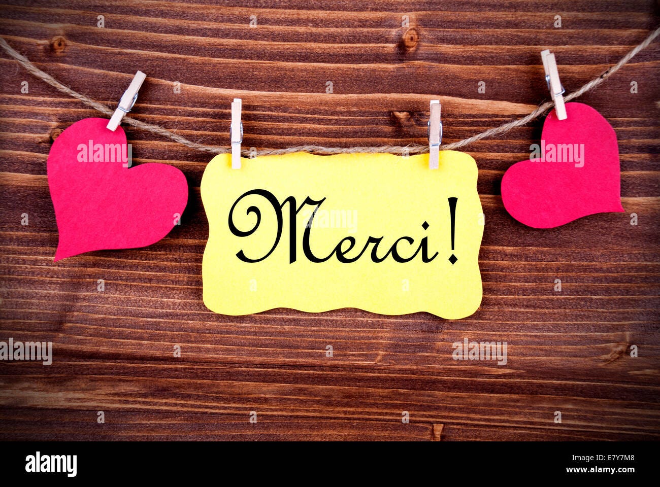 The French Word Merci, which means Thanks, on a Yellow Tag, framed by two  red Hearts hanging on a Line on Wood Stock Photo - Alamy