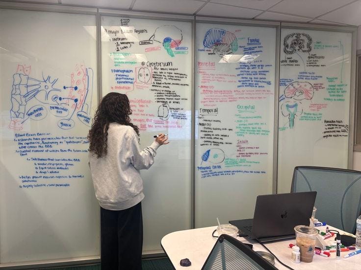 This may contain: a woman standing in front of a whiteboard with writing on it and looking at her cell phone
