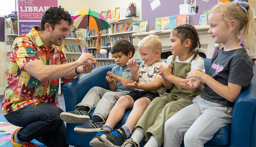 Chip in a library sharing a story with four engrossed children aged 5 to 9 Chip in a library sharing a story with four engrossed children aged 5 to 9