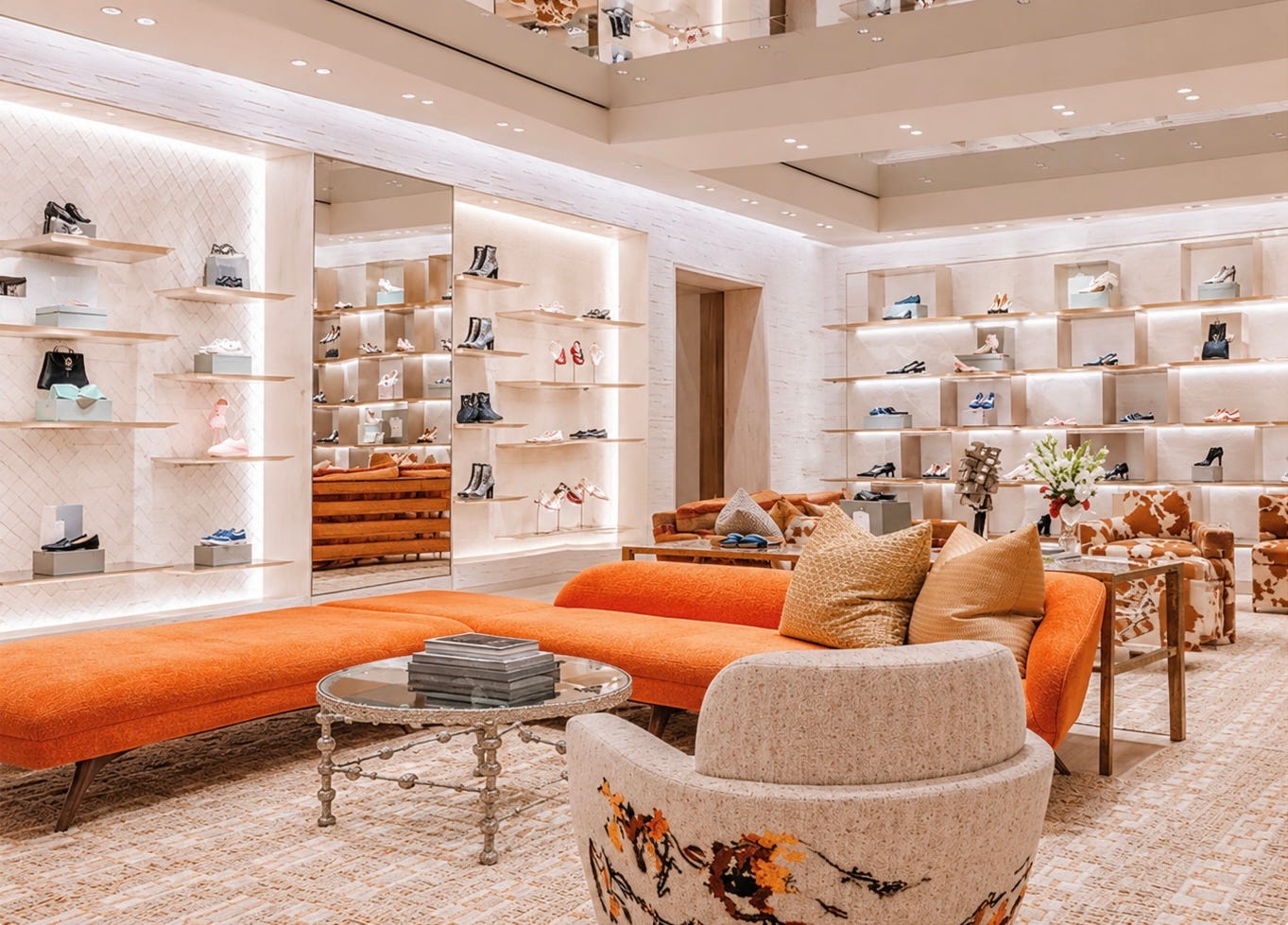 Dior boutique interior designed as an intimate lounge, with an orange sofa, upholstered seating, mirrored ceilings, and illuminated displays of shoes and accessories.