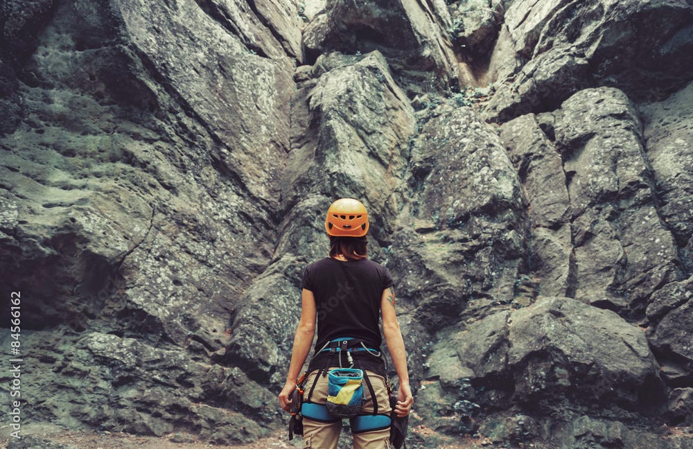 Climber woman standing in front of a stone rock outdoor