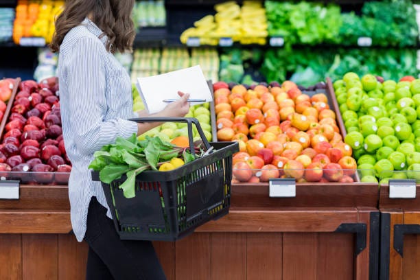 Unrecognizable woman shops for produce in supermarket Young woman carries a shopping basket filled with fresh produce. She is shopping for fresh fruit and vegetables in a grocery store. food retail stock pictures, royalty-free photos & images Unrecognizable woman shops for produce in supermarket Young woman carries a shopping basket filled with fresh produce. She is shopping for fresh fruit and vegetables in a grocery store. food retail stock pictures, royalty-free photos & images