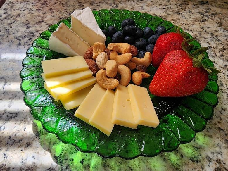A Supermodel Snack of brie, gouda, cheddar, unsalted mixed nuts, blueberries, and strawberries artfully arranged on a vintage green glass plate with excellent lighting. Sun is peeking through the blinds casting an interesting shadow on the faux granite countertop beneath it. A Supermodel Snack of brie, gouda, cheddar, unsalted mixed nuts, blueberries, and strawberries artfully arranged on a vintage green glass plate with excellent lighting. Sun is peeking through the blinds casting an interesting shadow on the faux granite countertop beneath it.
