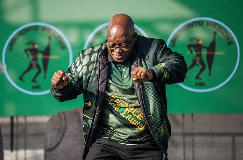 A man dances on stage wearing MK Party regalia. A man dances on stage wearing MK Party regalia.
