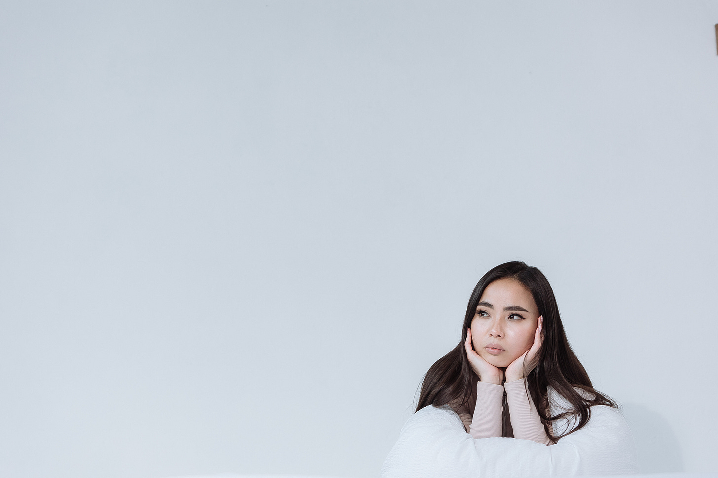 A woman sits in the bottom left corner of the screen with her chin in her hands. She looks like she's thinking. There's a gray background behind her.