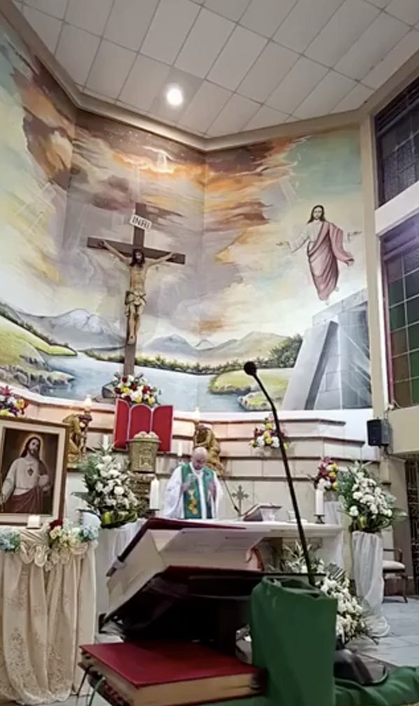 A priest says Mass at an altar in a church. A large wooden crucifix is on the wall behind him. A priest says Mass at an altar in a church. A large wooden crucifix is on the wall behind him.
