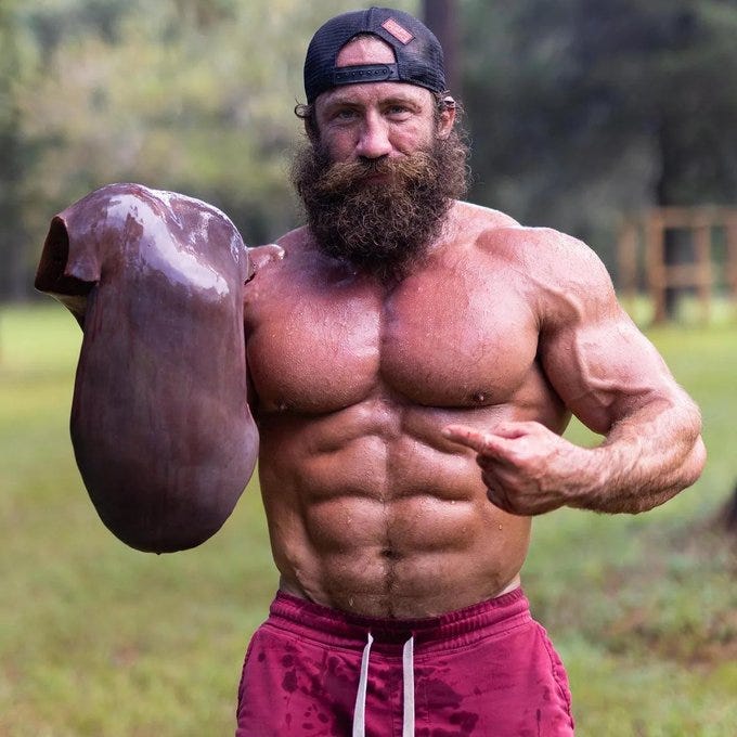 Brian Johnson, o Liver King, segura um fígado cru na mão esquerda, e está sem camisa e usando um boné