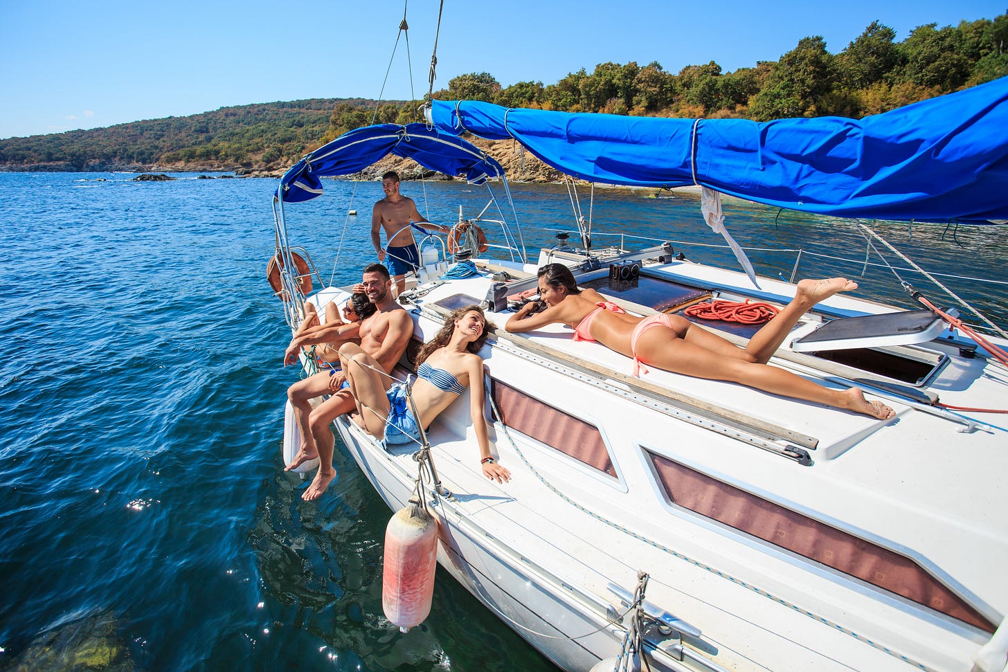 Twentysomething people, about 5 of them,sunning themselves on a yacht off a lush green island