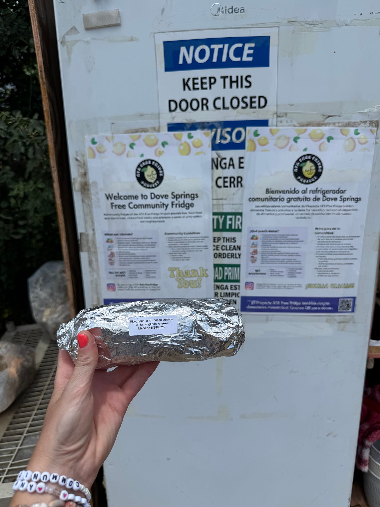 a hand holding a packaged burrito in front of a community fridge