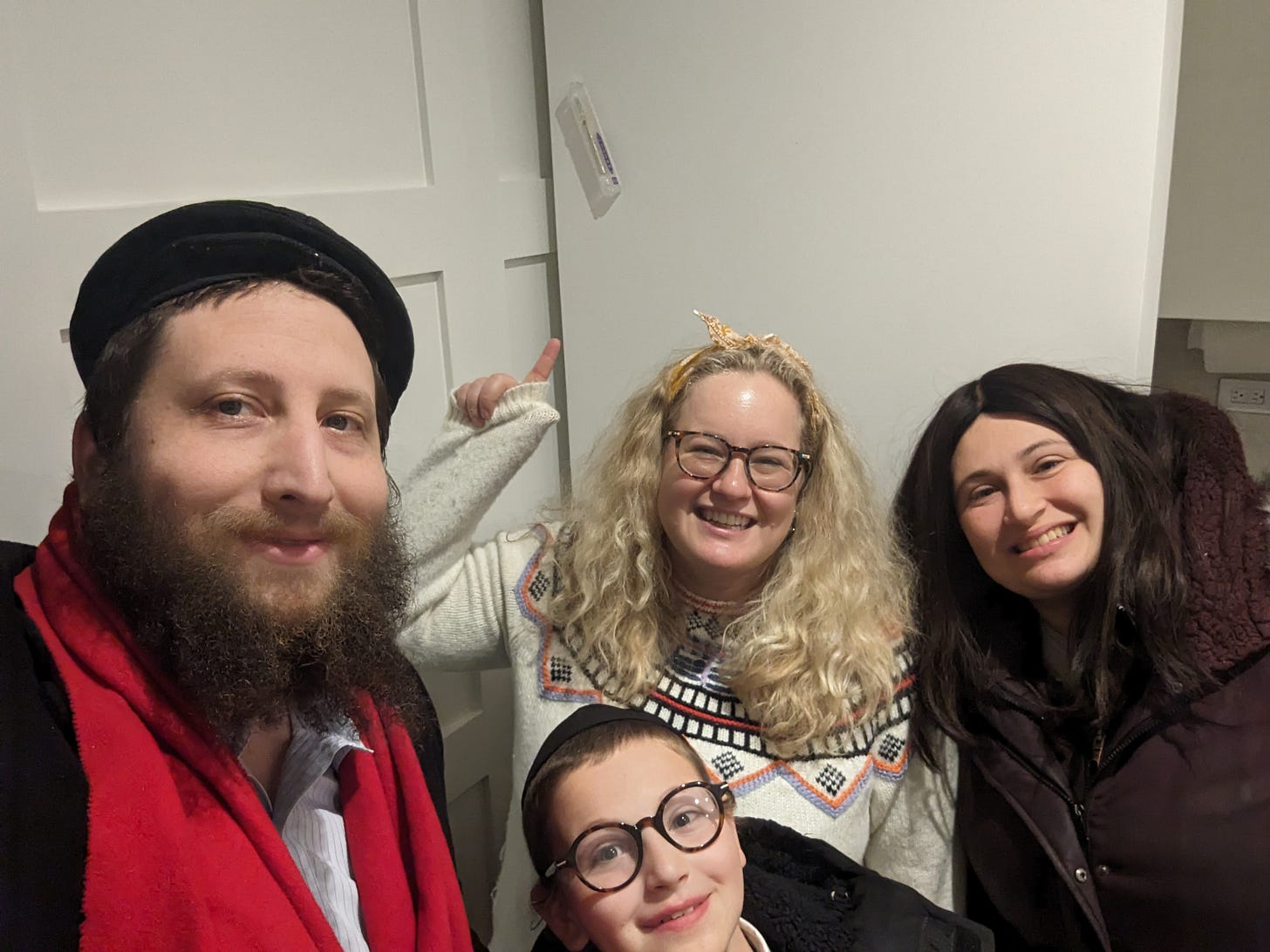 a rabbi in a red scarf helps a lady put up a. mezuzah while his wife and son join in.