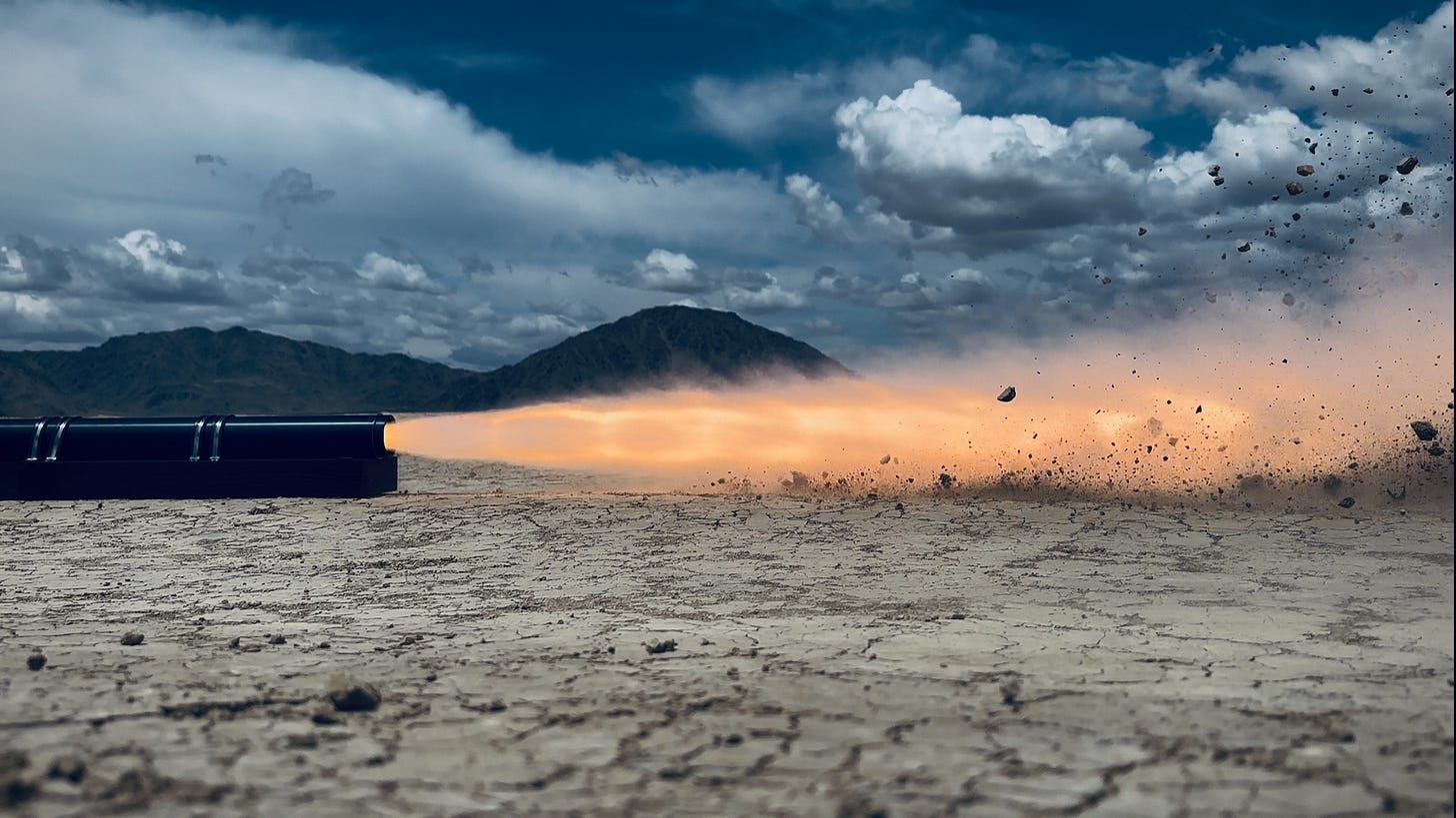 Solid rocket motor hotfire on a Mojave dry lake bed, with a long orange plume cutting across the cracked white playa under stormy blue sky. Solid rocket motor hotfire on a Mojave dry lake bed, with a long orange plume cutting across the cracked white playa under stormy blue sky.