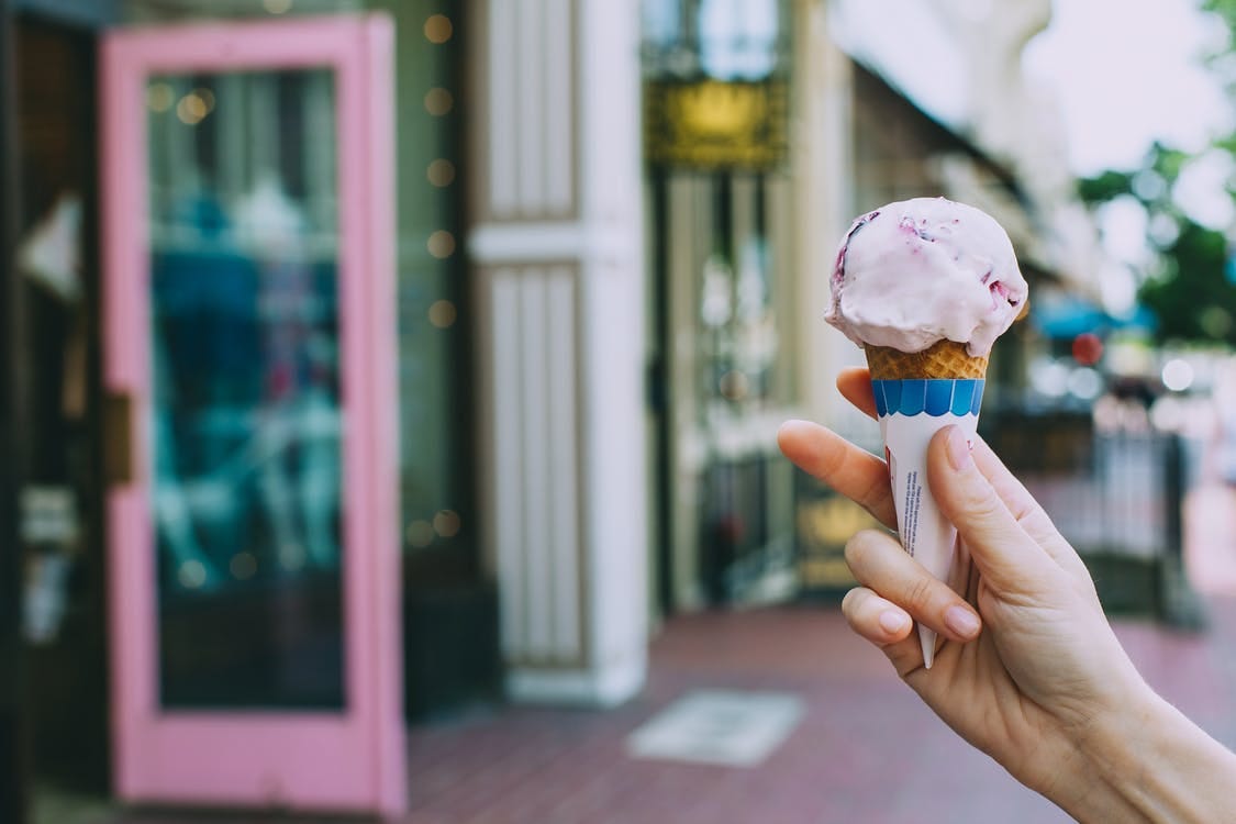 Crop person showing delicious ice cream cone on street