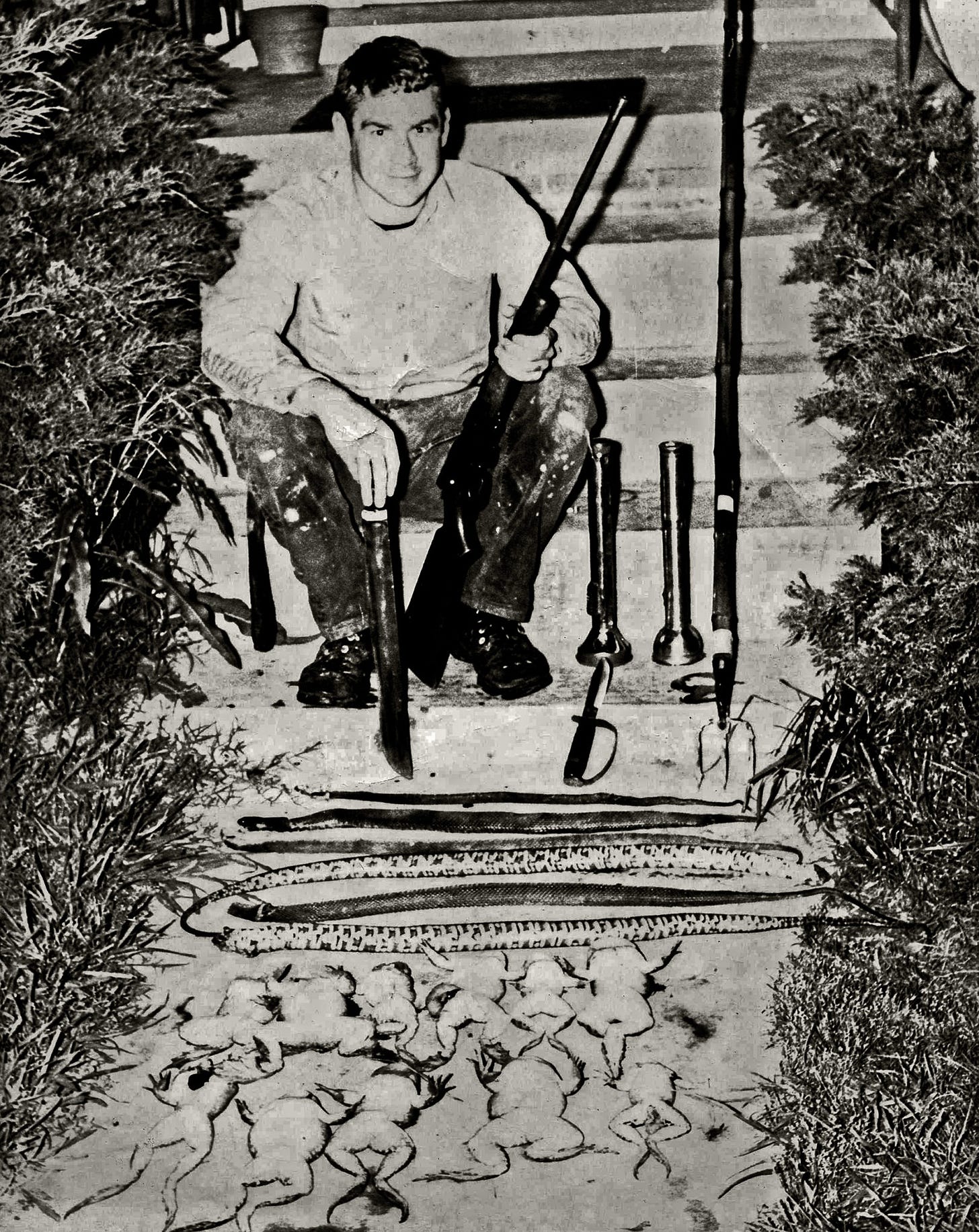 A boy sits with a rifle with a bunch of dead frogs.