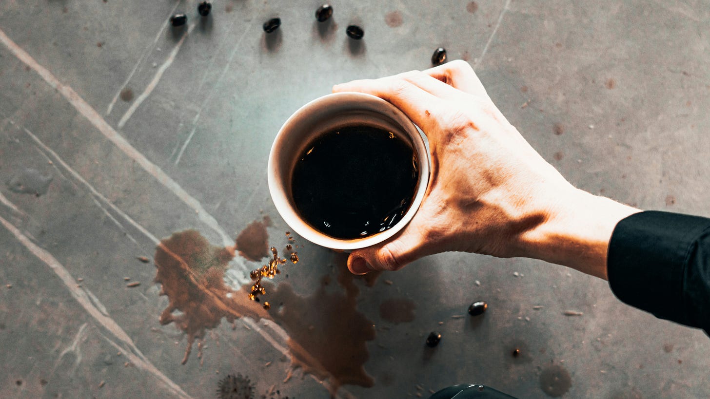 A hand holding a coffee cup, with some spilled and coffee beans scattered about A hand holding a coffee cup, with some spilled and coffee beans scattered about