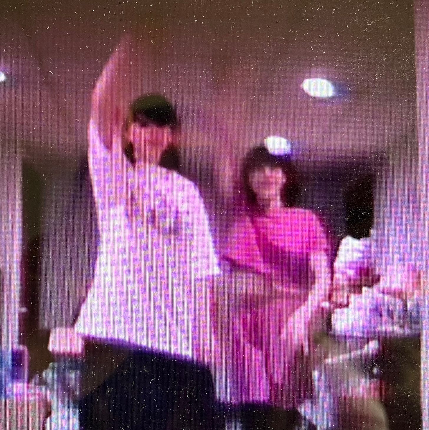 Blurry, grainy photo of two girls dancing in a very cluttered finished basement.