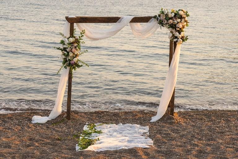 A wooden structure with white cloths and flowers on the beach

AI-generated content may be incorrect.