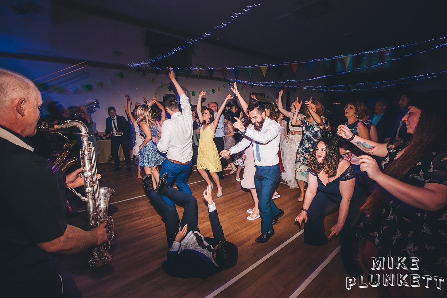 A large group of people dancing, arms in the air, smiles as music plays
