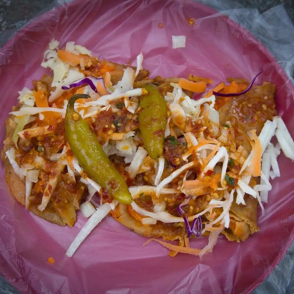 A plastic plate filled with tacos al vapor and smothered with salads and salsa