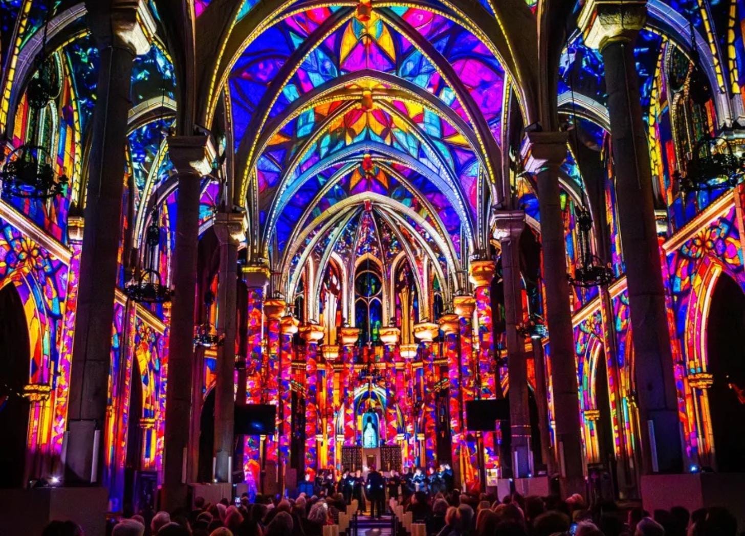 Nave of the Basilica of Notre-Dame de Nice flooded with red and blue projected light during the Luminescence show, audience seated in the pews facing the altar.