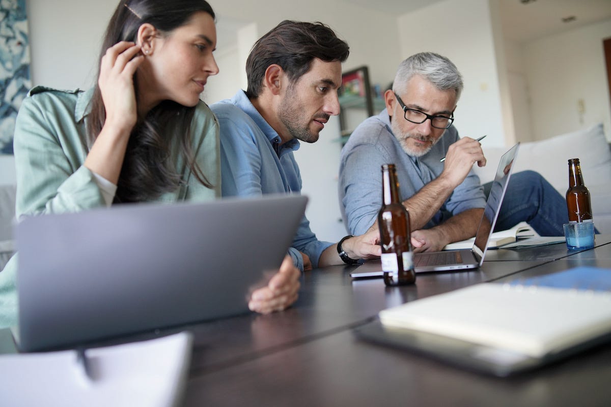 A group of people sitting at a table with a computer and a bottle of beer

Description automatically generated with medium confidence