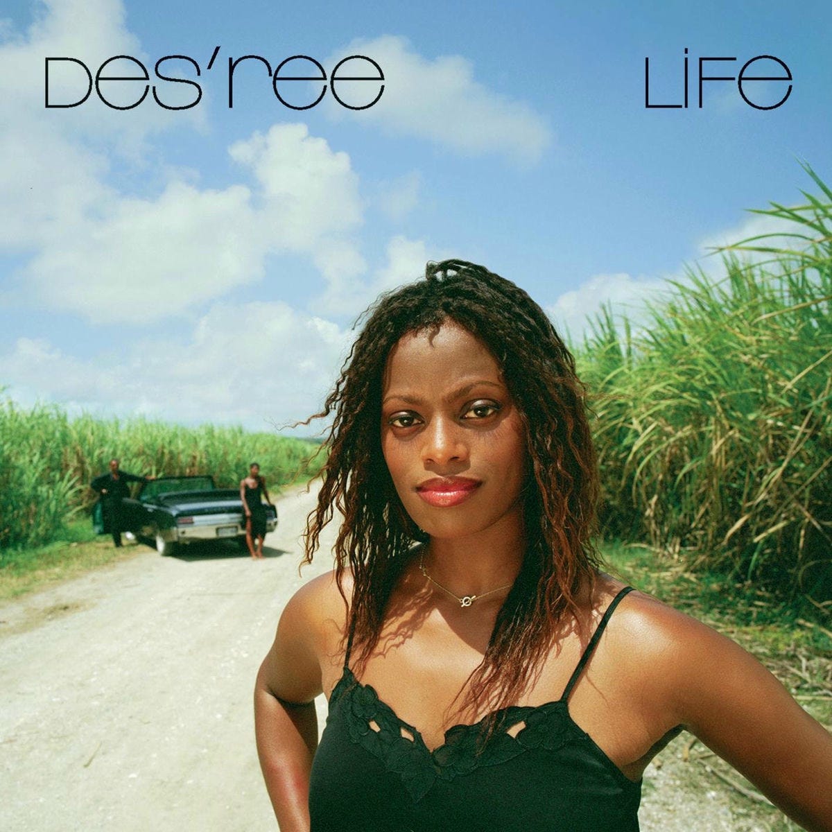 The album cover for Des'ree's single Life. It shows Des'ree, a black woman in her 20s with long, softly kinky hair, in the foreground, shown from the chest up with her hands on her hips, standing on a brightly lit dirt road under a blue sky, with what look like crops either side. In the background, there's an open-top convertible parked slightly off the road, with two black people standing close to it.