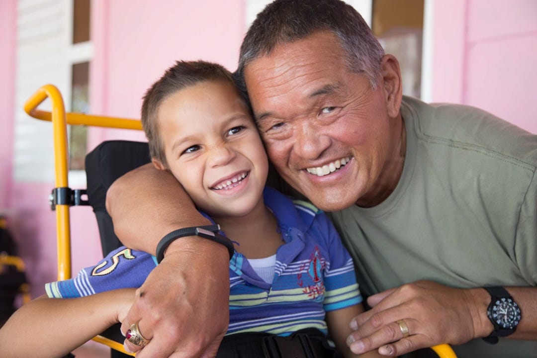 A Wheels for the World worker poses with a grinning child in need