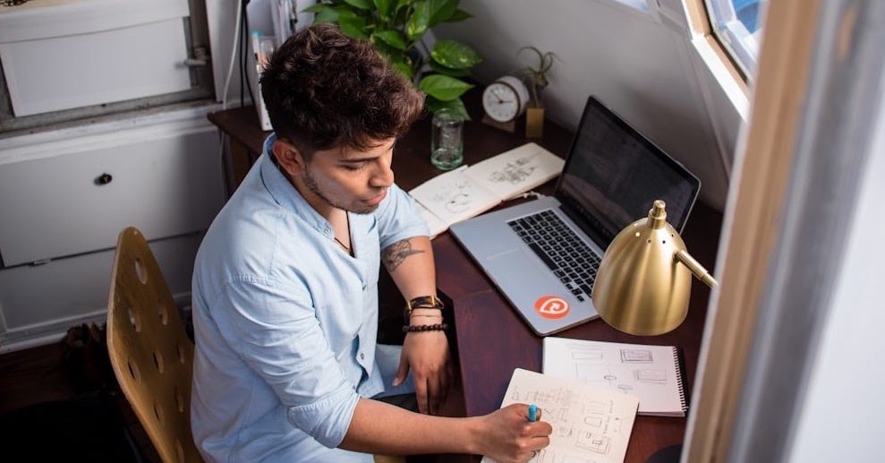 man sits while writing in front of MacBook man sits while writing in front of MacBook