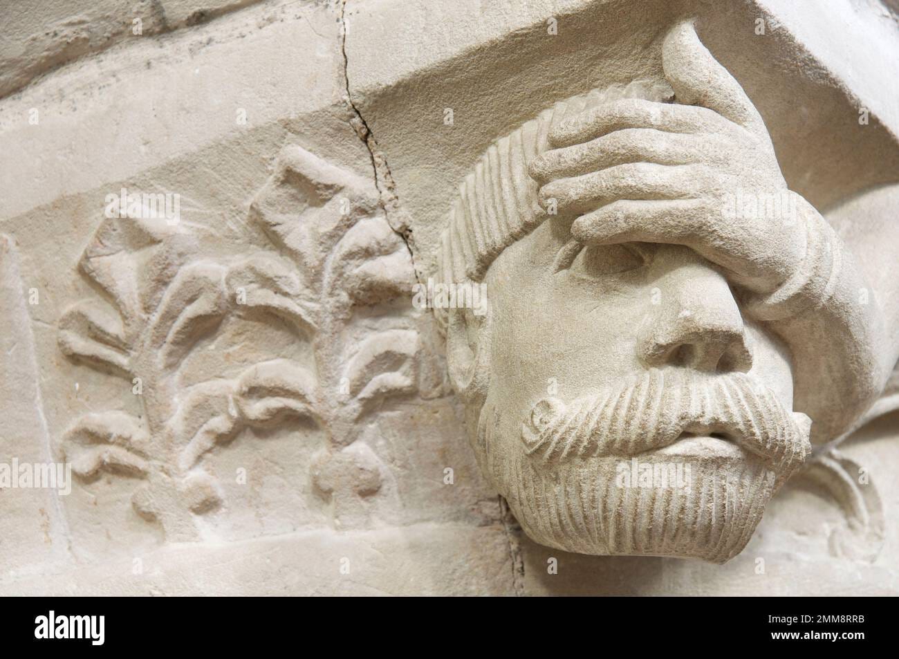 Carved stone grotesque head of a man apparently suffering from a headache,  on a 12th century pillar in St John the Baptist Church, Bere Regis, Dorset  Stock Photo - Alamy