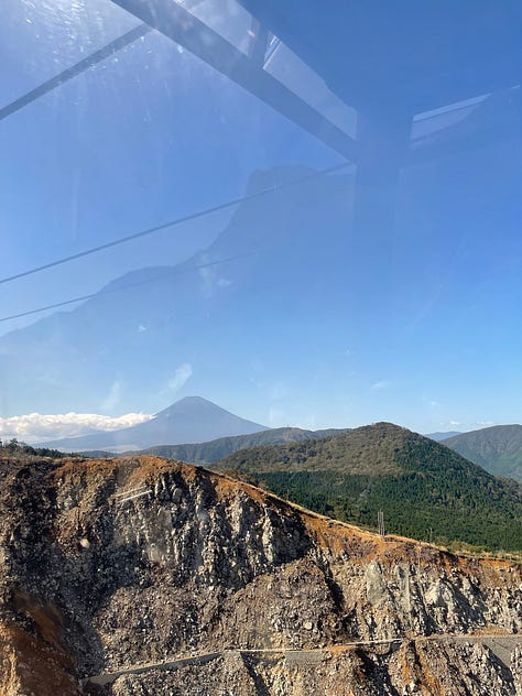 A collage of nine photos from Japan: a man in traditional kimono performing a tea ceremony; a tray of delicate kaiseki dishes with seasonal ingredients; a serene temple garden surrounded by moss and trees; a tatami room with sliding shoji doors; a mountain view with Mount Fuji in the distance; a bowl of Japanese dessert with green grapes and jelly; a Shinto wedding procession under a red umbrella; a moss-covered stone Buddha statue in a forest; and misty temple grounds framed by lush greenery.